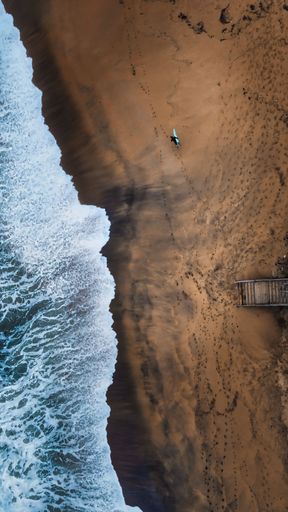 An aerial view of red rocks near the blue ocean with big waves
