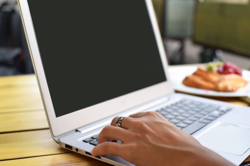 A closeup shot of a young female working on her laptop and having a croissant in a cafe