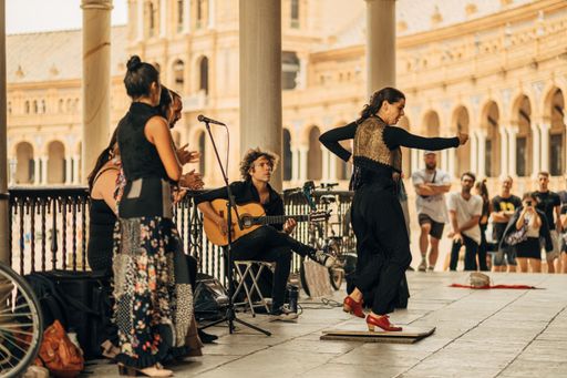 A daytime view of a young female performing a dance with musicians playing in front of a crowd in Sevilla, Spain