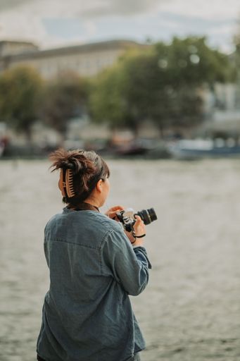 A vertical shot of a young female taking pictures of a river during daytime in Paris, France