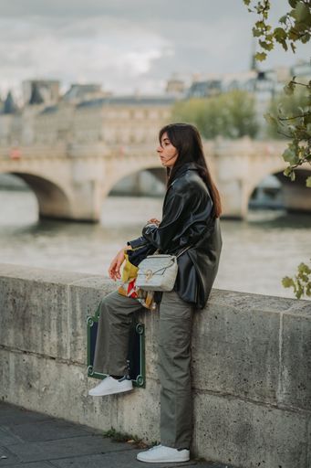 A vertical shot of a young woman sitting on the bridge in Paris, France