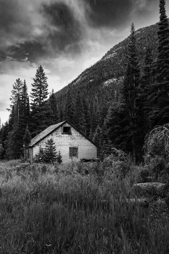 An old house on a field against a hill and a cloudy sky in the countryside, Grayscale shot