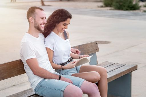 A young Caucasian couple sitting on a bench and reading a book