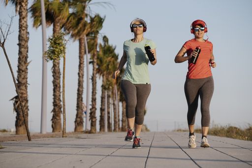 A shallow focus of two young females in sportswear with headphones jogging in a park