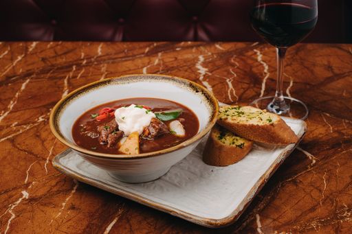 A closeup shot of a Hungarian soup with garlic bread on the table with red wine
