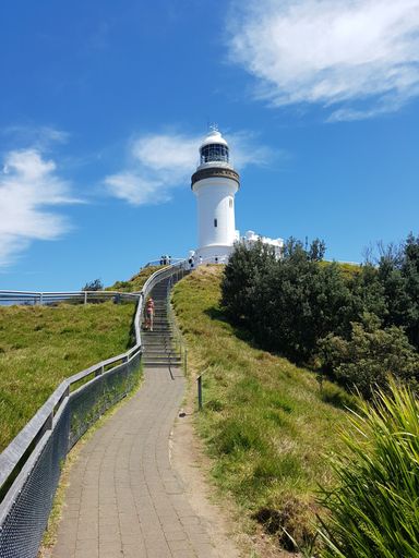 A vertical low-angle of path leading to the Cape Byron lighthouse, grass on both sides, cloudy sky background
