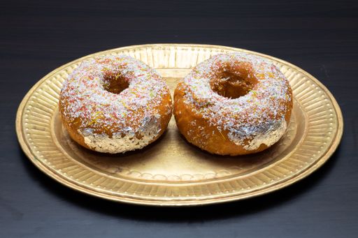 A closeup of two donuts with sprinkles on them on a gold plate with a black background
