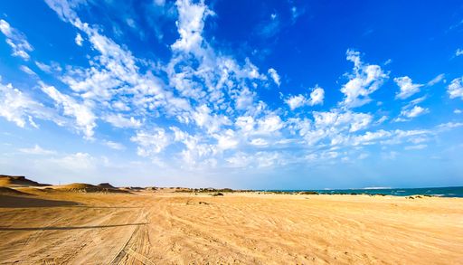 A scenic view of a sandy beach against the sea in United Arab Emirates under a cloudy blue sky