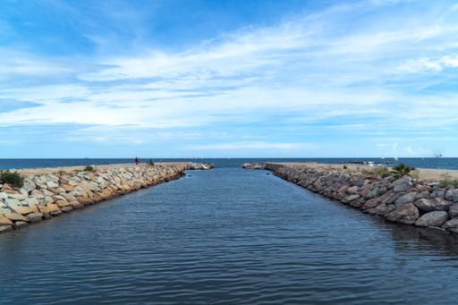 A natural view of a calm river flowing to the sea under a wispy sky