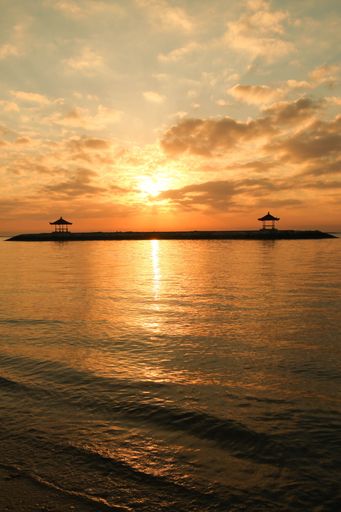 A vertical shot of a seascape under a cloudy sunset sky with silhouettes of gazebos in the background