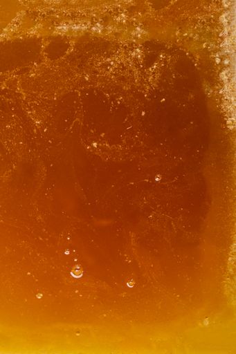 Liquid thick orange-golden bee honey in container. Textured surface with air bubbles. Delicious and healthy natural food.