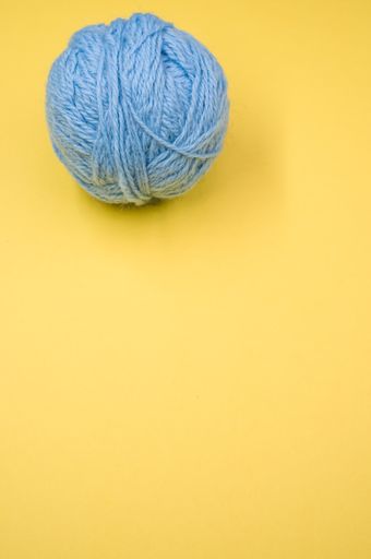 A vertical shot of a ball of blue yarn on a yellow surface