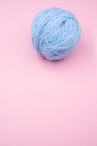 A vertical shot of a ball of blue yarn on a pink surface