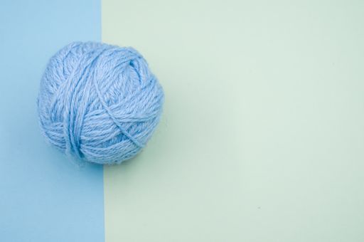 A high angle shot of a ball of blue yarn on a blue surface