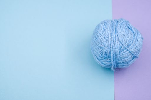 A high angle shot of a ball of blue yarn on a blue surface