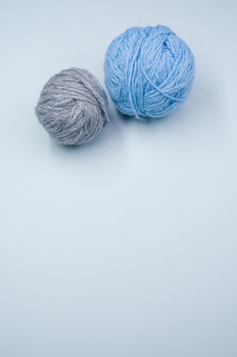 A vertical shot of two balls of yarn on a blue surface