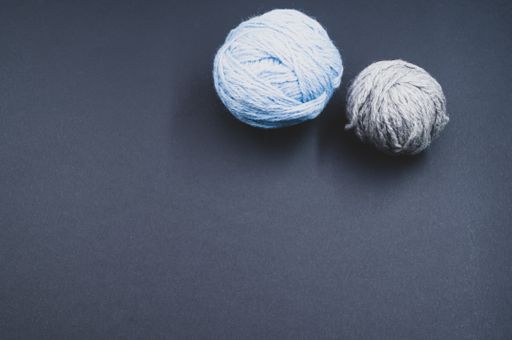 A high angle shot of two balls of yarn on a blue surface