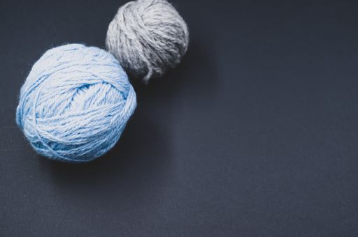 A high angle shot of two balls of yarn on a blue surface
