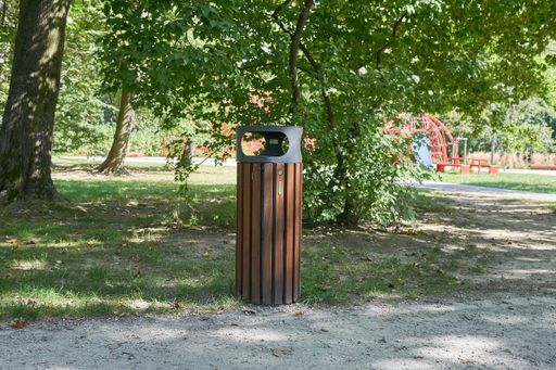 A garbage bin surrounded by greenery in a park under the sunlight with a blurry background