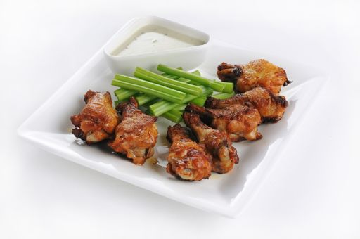 An isolated shot of a white plate with chicken legs with sauce - perfect for menu usage