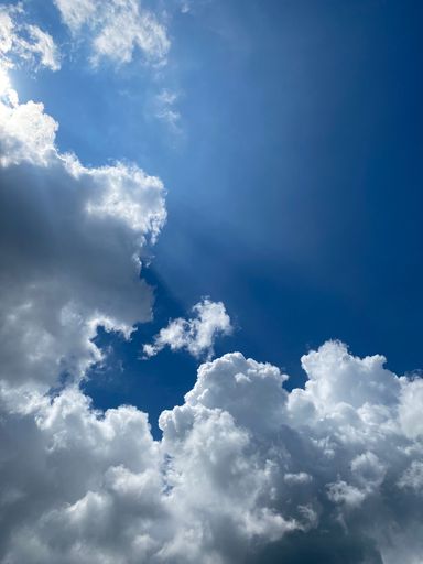 A vertical shot of a a beautiful bright blue sky with rainstorm clouds and sunbeams.