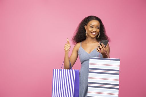 A pretty black lady carrying some shopping bags gives a thumbs up.