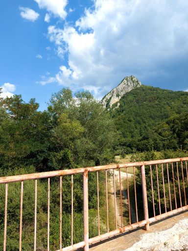 A metal bridge over the river with a background of high mountains, vertical
