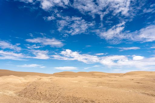 A landscape of a deserted area captured below the blue sky with a scattered cloudscape