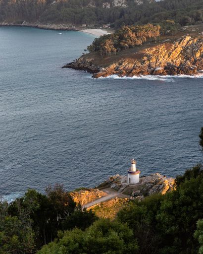 An aerial view of sea breaking rocky beach with lighthouse in Ilhas Cies