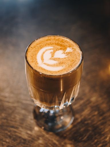 A vertical shot of latte art in a glass cup of coffee placed on a wooden table.