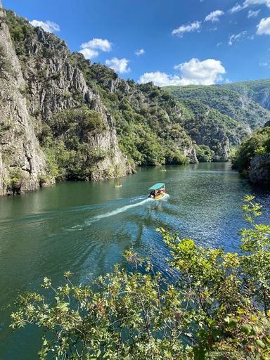 A vertical shot of the river with a boat surrounded by green cliffs.