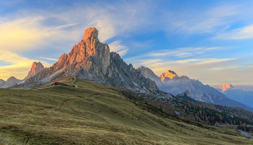 A breathtaking view of rocky cliffs overlooking a solitary cabin in the hills under a colorful sky