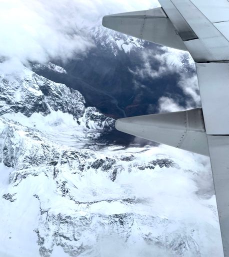 A vertical shot of a lake and snow covered mountains seen from an airplane