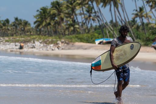 An Indian Male with his Surf Board walking by the Sea Shore