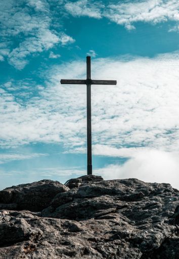 A vertical shot of the cross on the top of the stony hill against a blue sky