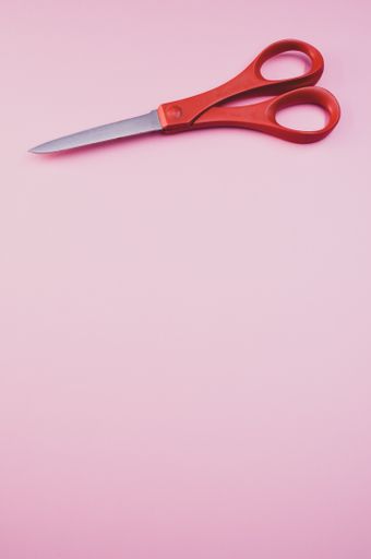 A vertical shot of a pair of sewing scissors on a pink surface