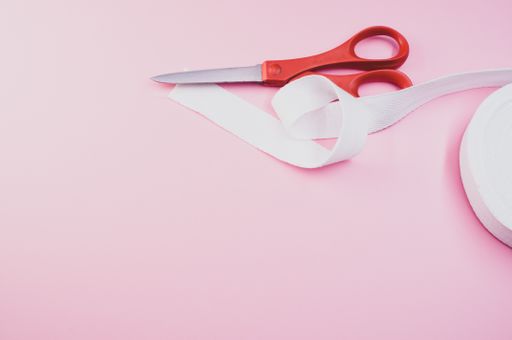 A high angle shot of scissors and a ribbon on a pink surface