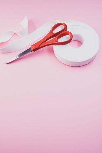 A vertical shot of scissors and a ribbon on a pink surface