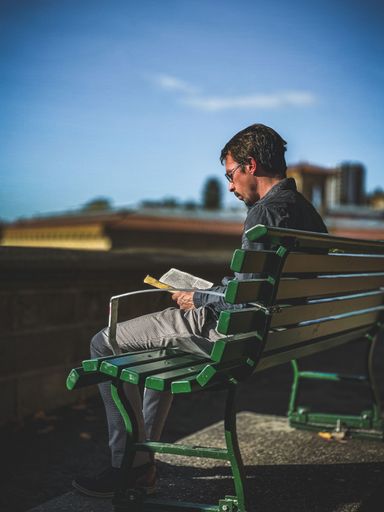 A vertical shot of a man reading a book on a bench in Lausanne, Geneva, Switzerland