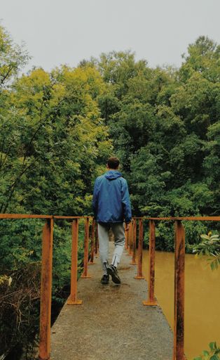 A vertical shot of a young man walking on a bridge to a forest
