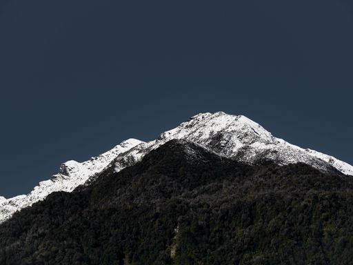 A scenic view of an evergreen mountain with snow on the top against a blue sky in New Zealand