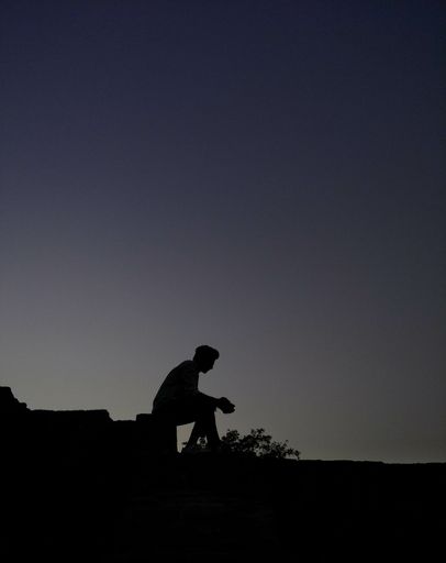 A vertical shot of a silhouette of a person sitting on a roof during evening time