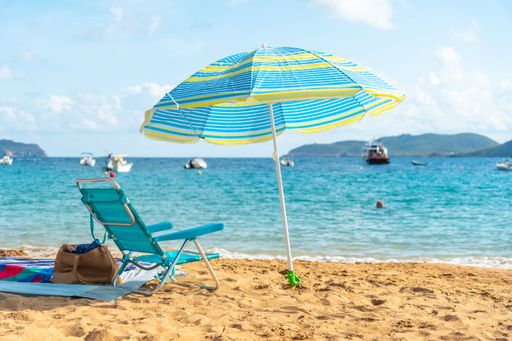 A paradisiacal beach with a blue umbrella in the sand overlooking the bright sea - summer vacation concept