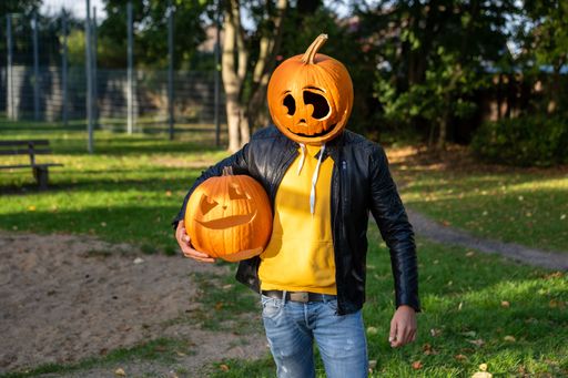 A female with a pumpkin head posing on the orange flowers under cloudy sky, vertical shot