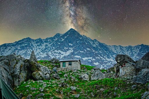 The houses on the slope of a green mountain with the Himalayas in the background