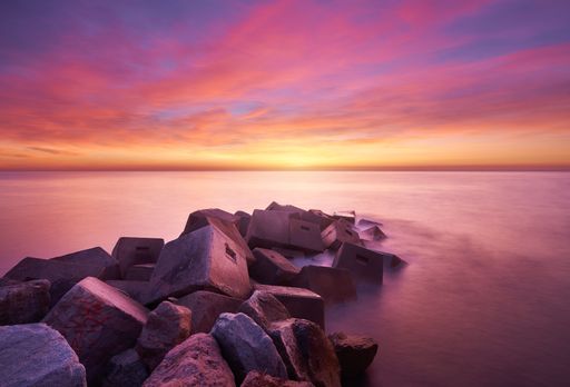 A dramatic shot of rocks by the sea at a pinky sunset