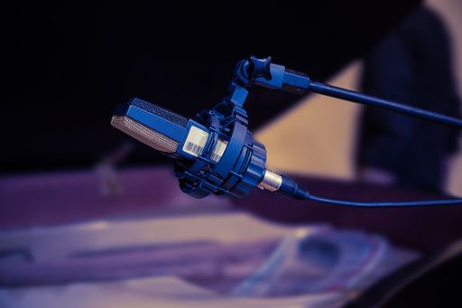 A closeup shot of a microphone on a mic stand with a piano on the blurred background
