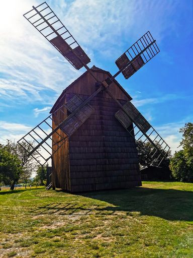 A low angle shot of a wooden windmill on a blue sky background