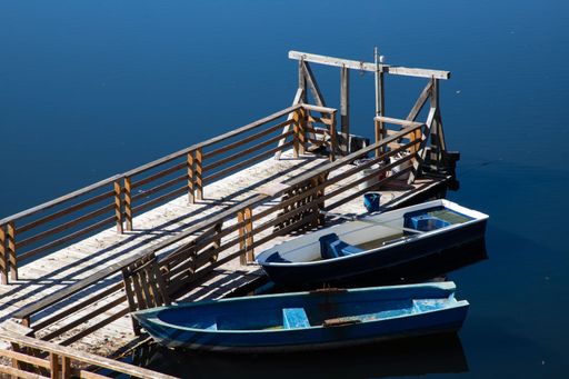 Two boats tied to a wooden pontoon on a clear blue body of water
