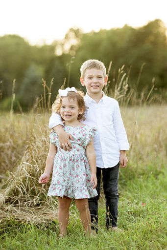 A vertical shot of a little brother hugging his sister while standing in a grassy field